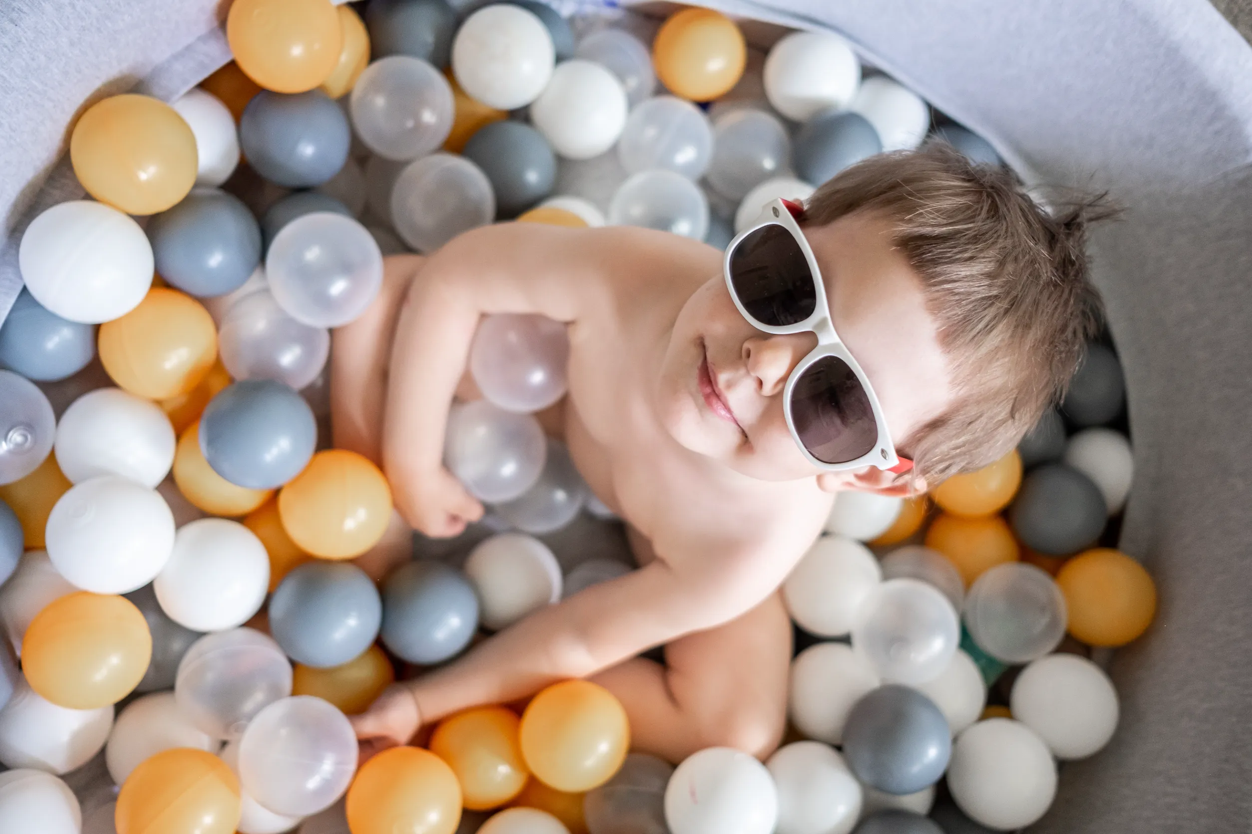 enfant portant des lunettes de soleil et nageant dans une piscine à balles